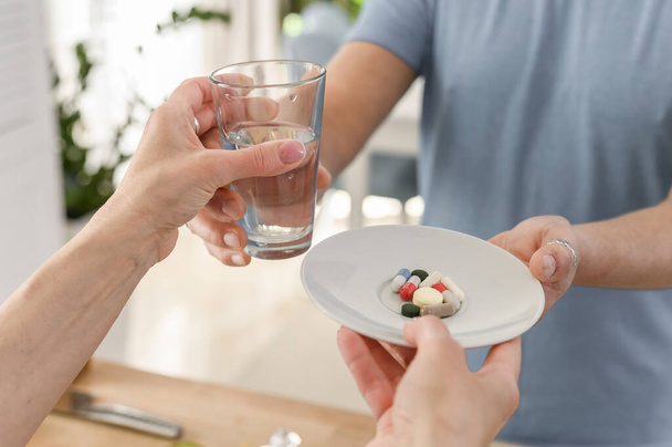Senior family taking food supplements pills before lunch with glass water. Close up cropped frame with hands - Фото, зображення