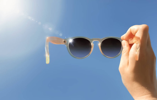 Female hand holds sunglasses against the blue sky. Outdoor close-up - Fotó, kép