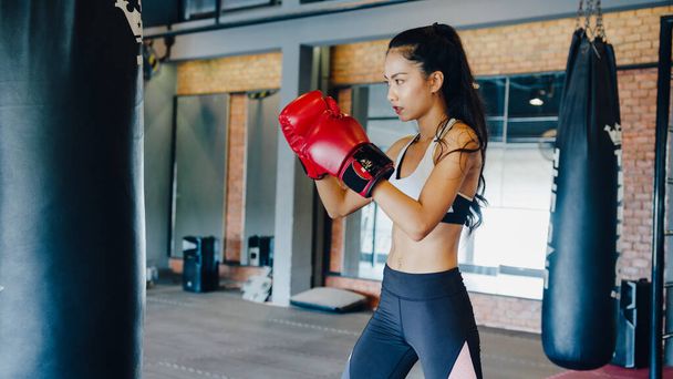 Νεαρή Ασιάτισσα κυρία kickboxing προπόνηση punching τσάντα σκληρή γυναίκα μαχητής πρακτική πυγμαχία στην τάξη γυμναστήριο. Αθλητική δραστηριότητα, λειτουργική κατάρτιση, έννοια του υγιεινού τρόπου ζωής. - Φωτογραφία, εικόνα