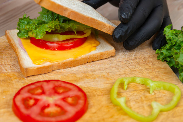 man in black gloves prepare sandwich on wooden desk - Фото, зображення