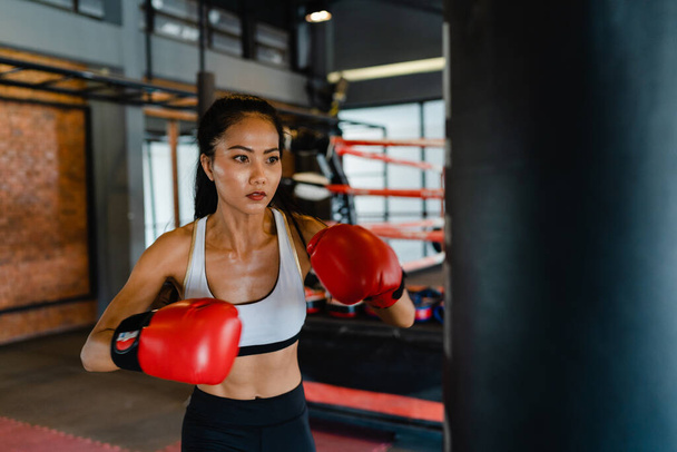 Young Asia lady kickboxing exercise workout punching bag tough female fighter practice boxing in gym fitness class. Sportswoman recreational activity, functional training, healthy lifestyle concept. - Foto, Imagen