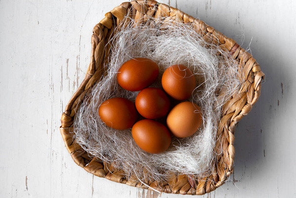 Brown chicken eggs in a wicker basket with straw - Foto, afbeelding