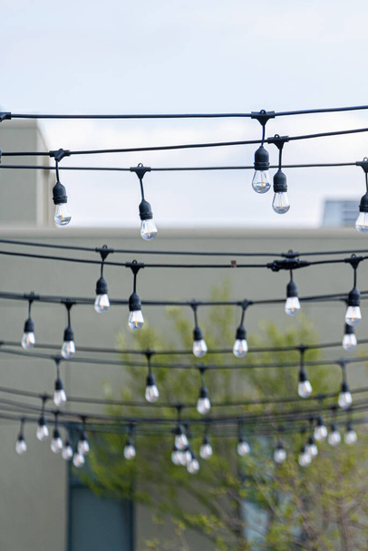 Струна электрических лампочек, натянутая на открытом патио ресторана - Фото, изображение
