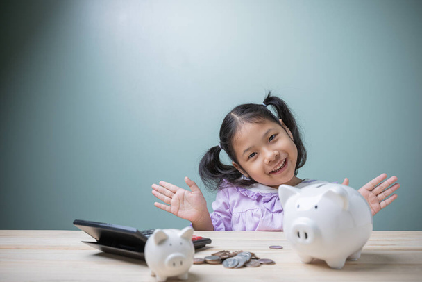 Мила азіатська дівчинка дуже щаслива, що заощаджує гроші на майбутнє зі свистячим банком, кусочками та калькулятором. Дитинство, необхідне для того, щоб навчитися заощаджувати гроші та освіту.. - Фото, зображення