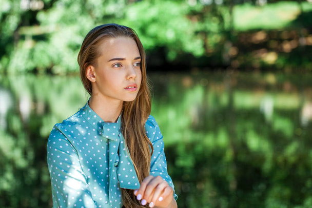Portrait of a young beautiful teenager girl in turquoise dress posing against the background of a pond in a summer park - Fotoğraf, Görsel