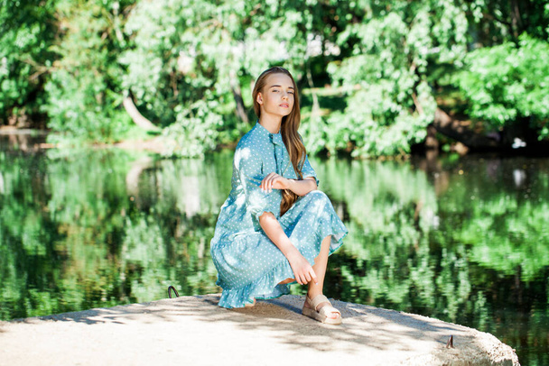 Portrait of a young beautiful woman in a lush turquoise dress posing against the background of a pond in a summer park - Fotoğraf, Görsel