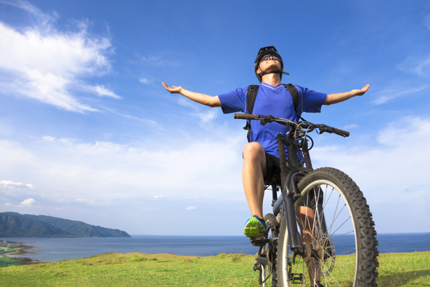 młody mężczyzna, siedzący na rowerze górskim i Otwórz ramiona do relaksu - Zdjęcie, obraz