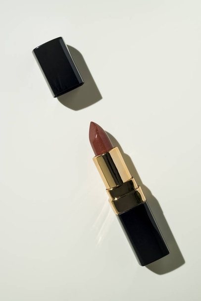 on a light beige background in the center of the frame, diagonally lies an open red with sequins lipstick in a black case with a gold stripe. the cap is next to it. mock up. - Foto, imagen
