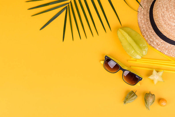 Carambola de frutas, accesorios de playa y follaje de una planta tropical sobre papel coloreado. Fondo de verano con estrellas de mar y frutas - Foto, Imagen