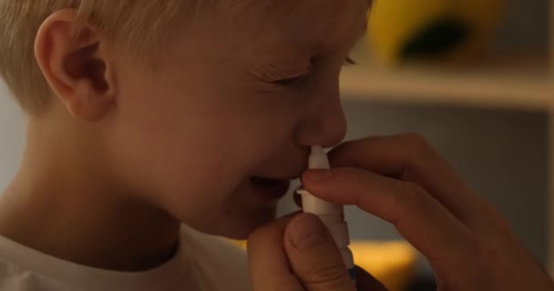 La mano de las mujeres inyecta un aerosol nasal a un niño rubio. Procedimientos de higiene en casa. Luz natural. Primer plano - Metraje, vídeo