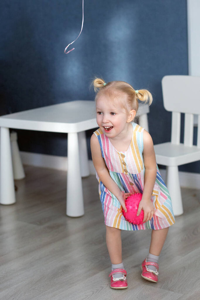 Blond toddler girl in dress playing with ball at home. Kid having fun at birthday party. Vertical - Φωτογραφία, εικόνα