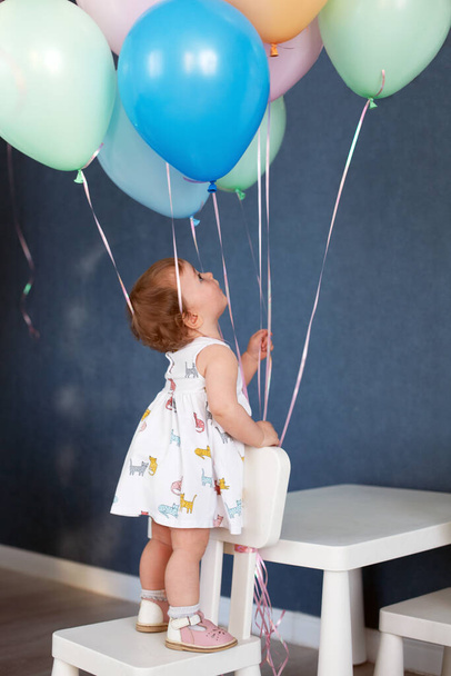 カラフルな風船を見てドレスを着てかわいい1歳の女の子。誕生日のお祝い。垂直 - 写真・画像