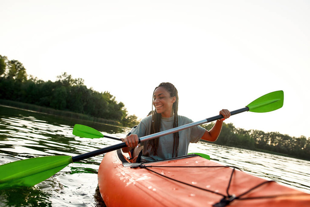 Joyful young woman smiling, enjoying a day kayaking together with her friend in a lake on a late summer afternoon - Photo, Image