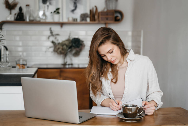 ノートパソコンのコーヒーを飲みながら家で働く笑顔の女性遠隔教育 - 写真・画像