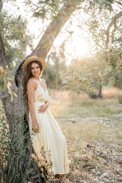 Tender portrait of beautiful brunette woman in beautiful sunlight. Woman in yellow summer linen dress in olive tree garden. Natural beauty.Travel to Italy, summer vacation - 写真・画像