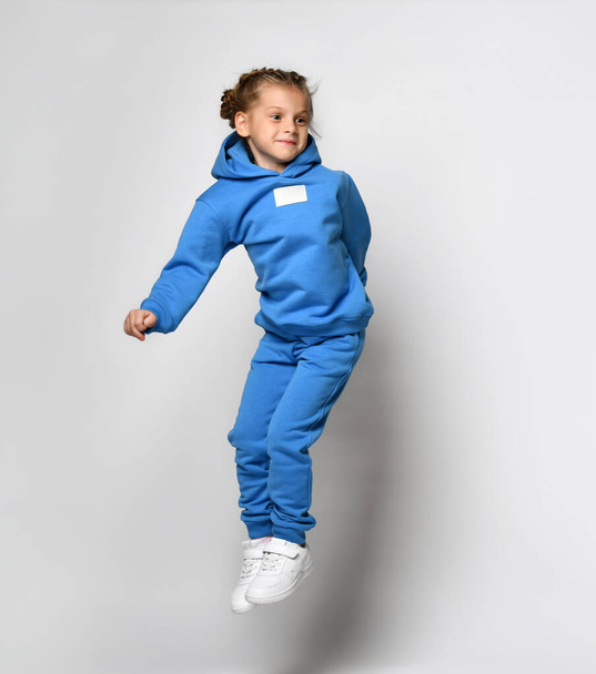 Playful cheerful girl in a stylish modern sports hoodie and pants jumps high. - Zdjęcie, obraz