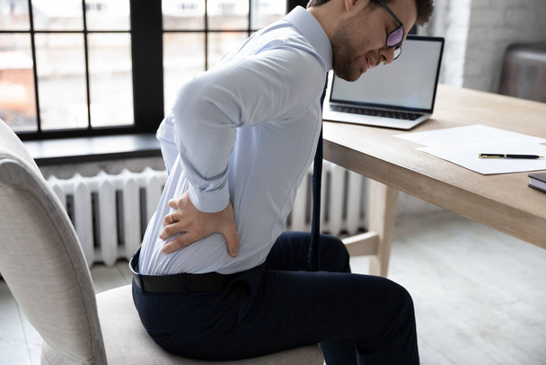 Upset young office employee suffering from chronic backache - 写真・画像