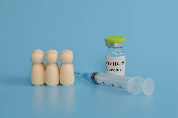 wooden doll figures of people, syringe and covid-19 vaccine on blue background. - Фото, изображение