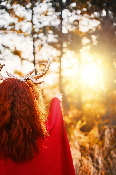 Hosszú piros ruhás nő szarvas szarvakkal az őszi erdőben. - Fotó, kép