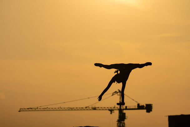 Silhouette of flexible acrobat doing handstand on the dramatic sunset background. Concept of willpower, control and dream - Foto, afbeelding