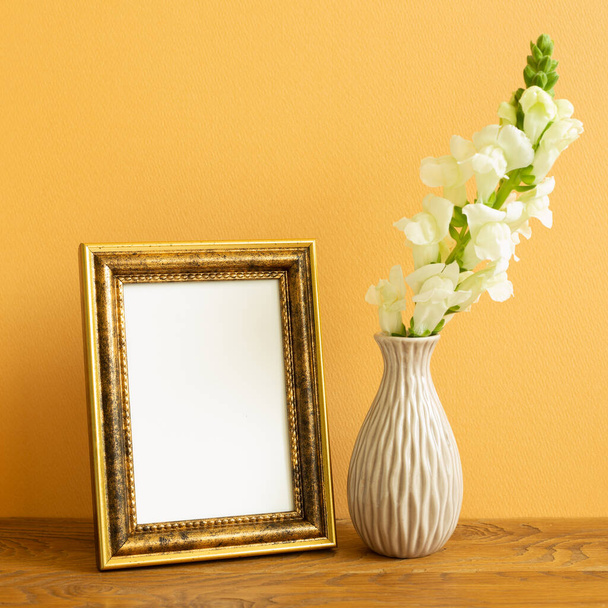 Pusta ramka na zdjęcie z kwiatami migawki na drewnianym stole. pomarańczowe tło - Zdjęcie, obraz
