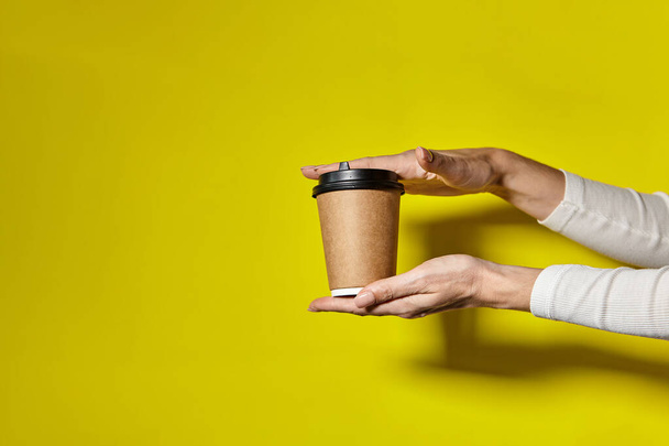 Hands holding two cups brown paper with black lid. Two coffee special offer or promo. Hands holding two cups on yellow screen background. Tea or Coffee to go. Brown paper cup with black lid. - Photo, Image