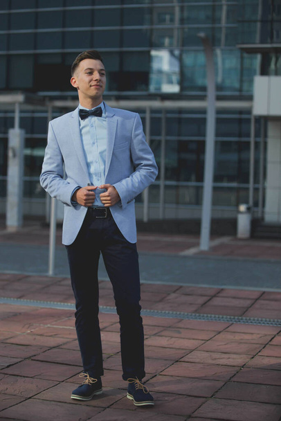 A vertical shot of a young male model posing in a light blue suit and a bow tie - Fotó, kép