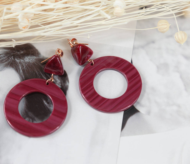  The red earrings are placed on the cardstock. The red earrings are decorated with light-colored lines. The shape of the earrings is a ring, and the material is very similar to stone. - Photo, Image