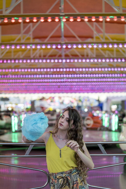 An attractive young female standing with cotton candy in hand and spending time in an amusement park - Foto, Imagen