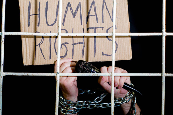le concept de liberté d'expression des droits de l'homme les mains liées par une chaîne de fer tiennent un microphone et une pancarte en carton portant l'inscription droits de l'homme derrière des barreaux de prison en fer. Photo de haute qualité - Photo, image