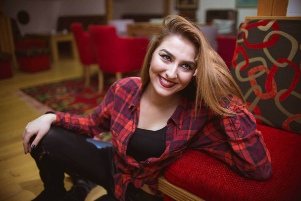 A shallow focus shot of a beautiful Bosnian Caucasian woman wearing a shirt and leather pants, sitting indoors - Zdjęcie, obraz