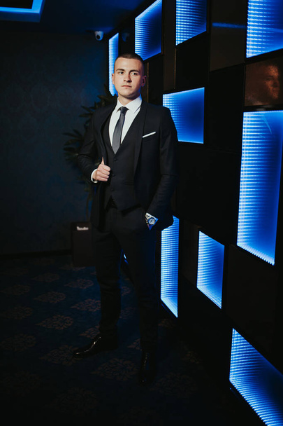 A vertical shot of a young attractive male in a formal suit posing in a nightclub - Фото, зображення