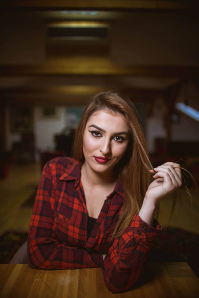 A vertical shot of a young blonde female in a black top and checkered shirt posing at home - Фото, изображение