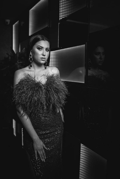 A vertical grayscale shot of a young attractive female in an elegant sexy dress posing in a nightclub - Φωτογραφία, εικόνα