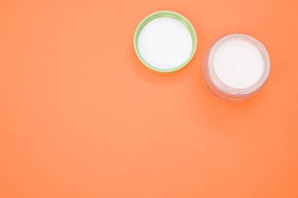 A top view of face cream in a small jar on an orange table with space for text - Fotoğraf, Görsel