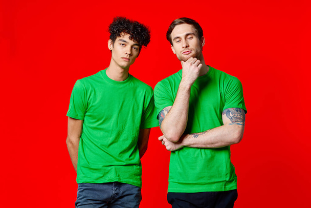 Yeşil tişörtlü iki arkadaş iletişim yaşam tarzı kırmızı arka plan - Fotoğraf, Görsel
