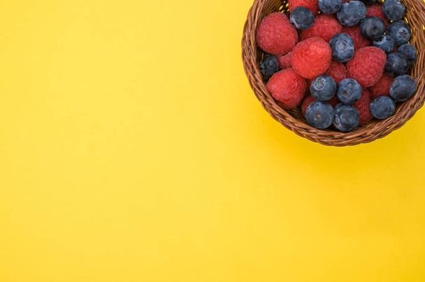 A top view of fresh raspberries and blueberries in a basket isolated on yellow background - Fotoğraf, Görsel