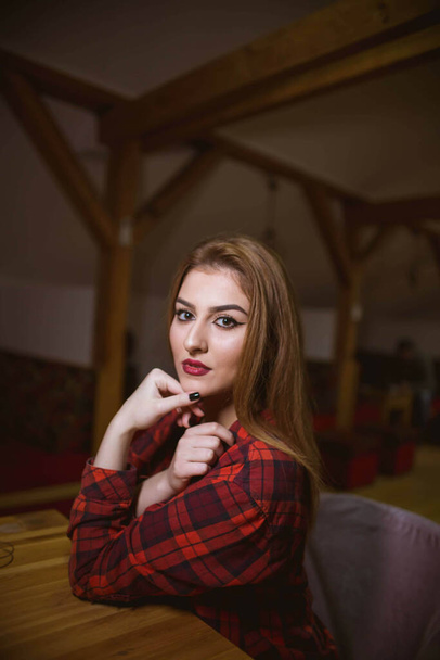 A vertical shot of a beautiful Bosnian Caucasian woman wearing a shirt and jeans, sitting indoors - Фото, изображение