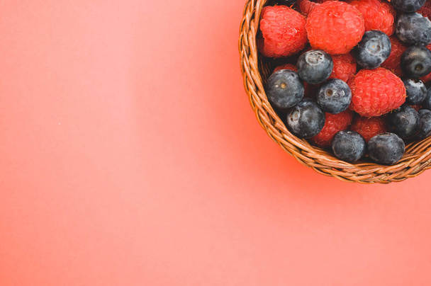 A top view of fresh raspberries and blueberries in a basket isolated on redbackground - Photo, Image