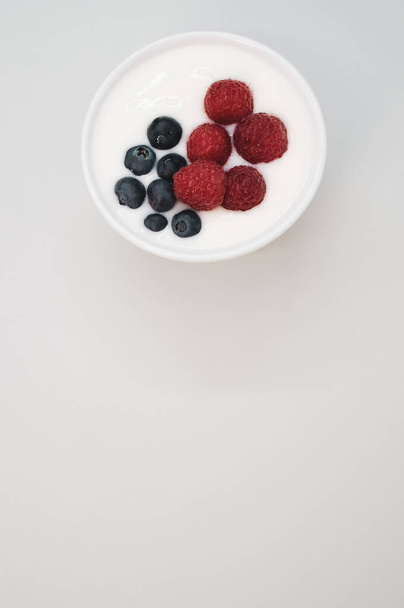 A closeup shot of a ceramic bowl of white yogurt with blueberries and raspberries - Foto, immagini