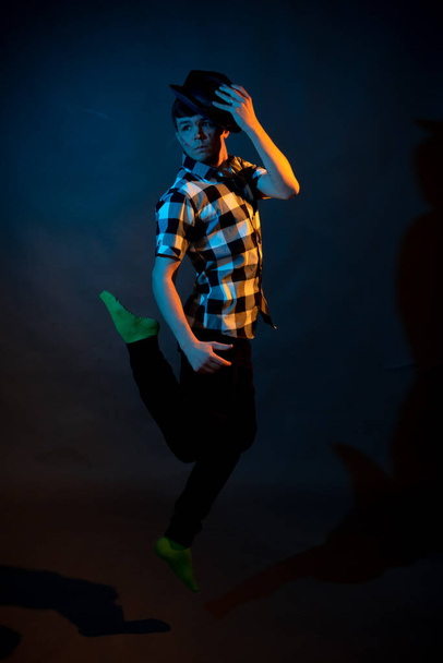 A young man in a plaid shirt jumps on a dark background illuminated by blue and yellow light - Фото, изображение
