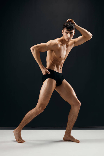 sportlicher Mann in schwarzen Shorts posiert auf dunklem Macho-Hintergrund - Foto, Bild