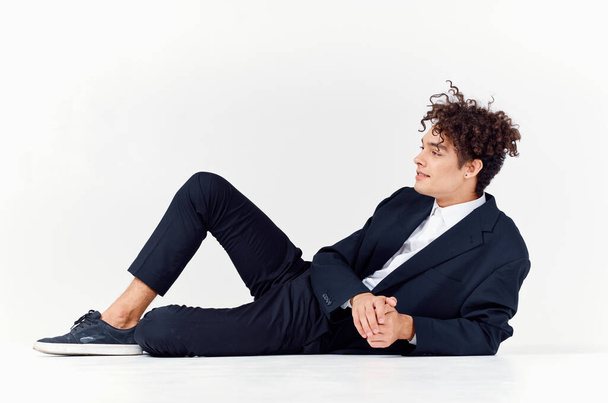 a fashionable guy in trousers and a jacket lies on the floor In a bright room, curly hair sneakers - Photo, Image