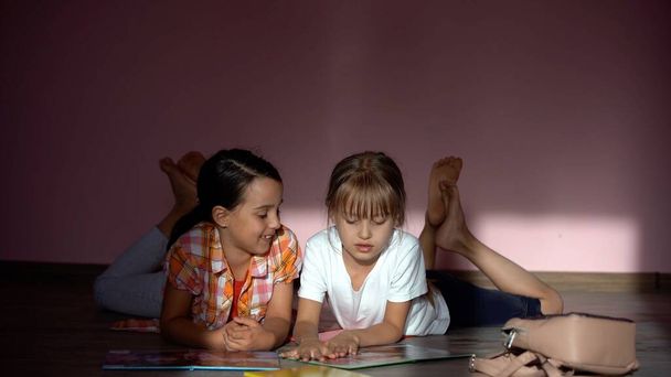 Dziewczynki czytające książkę w salonie. Mądre uczennice odrabiają lekcje po szkole. Edukacja i kształcenie na odległość dla dzieci. Nauka w domu podczas kwarantanny. Zostań w domu.. - Zdjęcie, obraz
