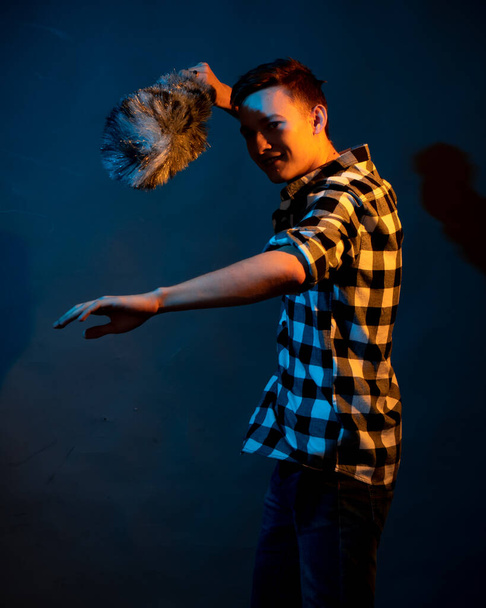 A guy in a plaid shirt with a dust brush on a dark background illuminated by blue and yellow light - Photo, image