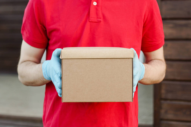 Close-up van de bezorger in rood uniform met kartonnen doos. Dienst in quarantaine. - Foto, afbeelding
