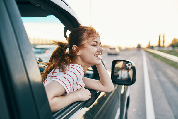 счастливая женщина на треке выглядывая из окна автомобиля в летние каникулы и туристический туризм - Фото, изображение
