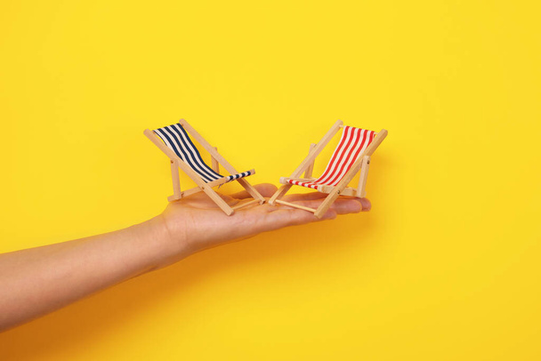 tumbonas de playa a mano, concepto de vacaciones de verano, tumbonas sobre fondo amarillo - Foto, Imagen