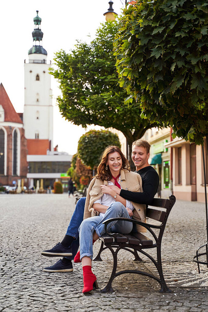 Beautiful young couple cuddling on a bench in a European town. Romatnic date and love concept. - Fotoğraf, Görsel