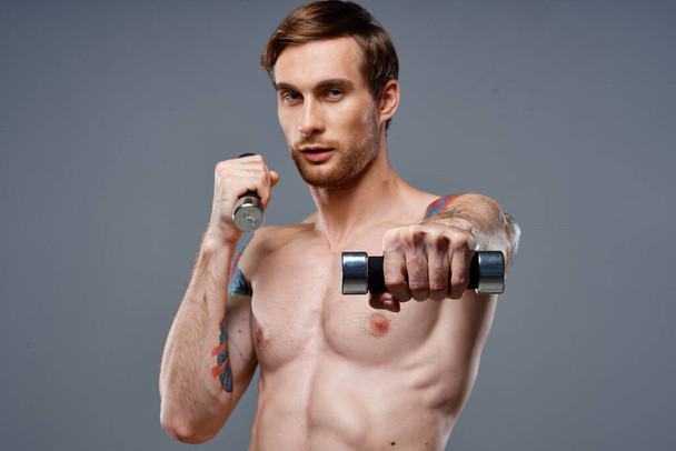 sportlicher männlicher Bodybuilder mit aufgepumpter Armmuskulatur und farbigem Tattoo-Kurzhantelbizeps - Foto, Bild
